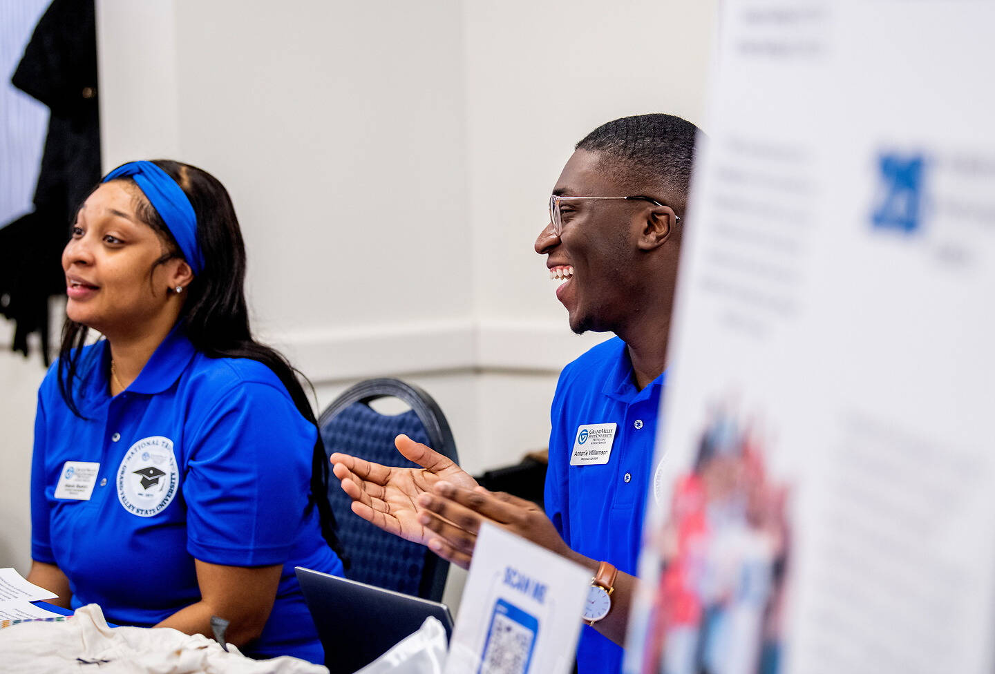 Two individuals in matching blue shirts engage in a lively conversation at an event booth.